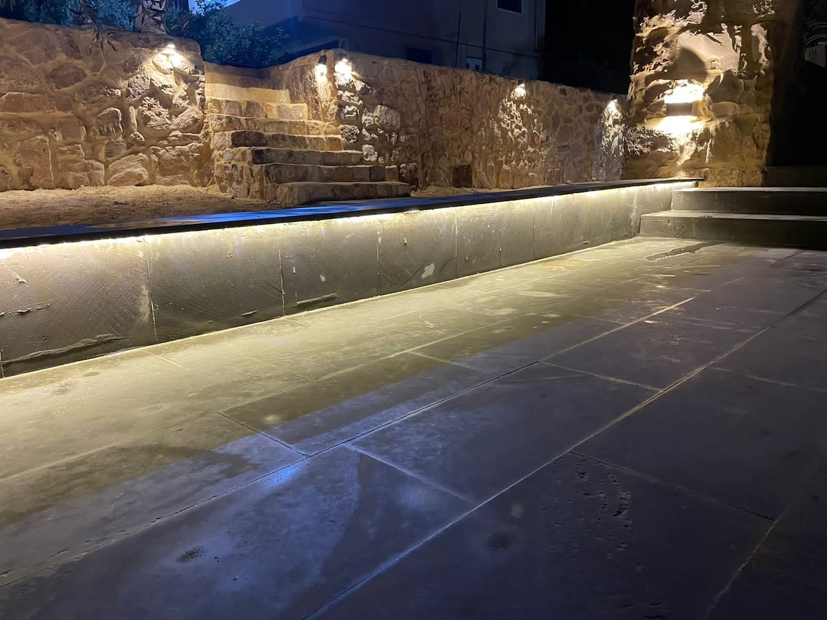 A sleek, flat stone surface is illuminated by subtle lighting, creating a warm glow. The surrounding stone walls add texture, while steps lead up toward the warm-toned rock, contributing to a calm and inviting ambiance.