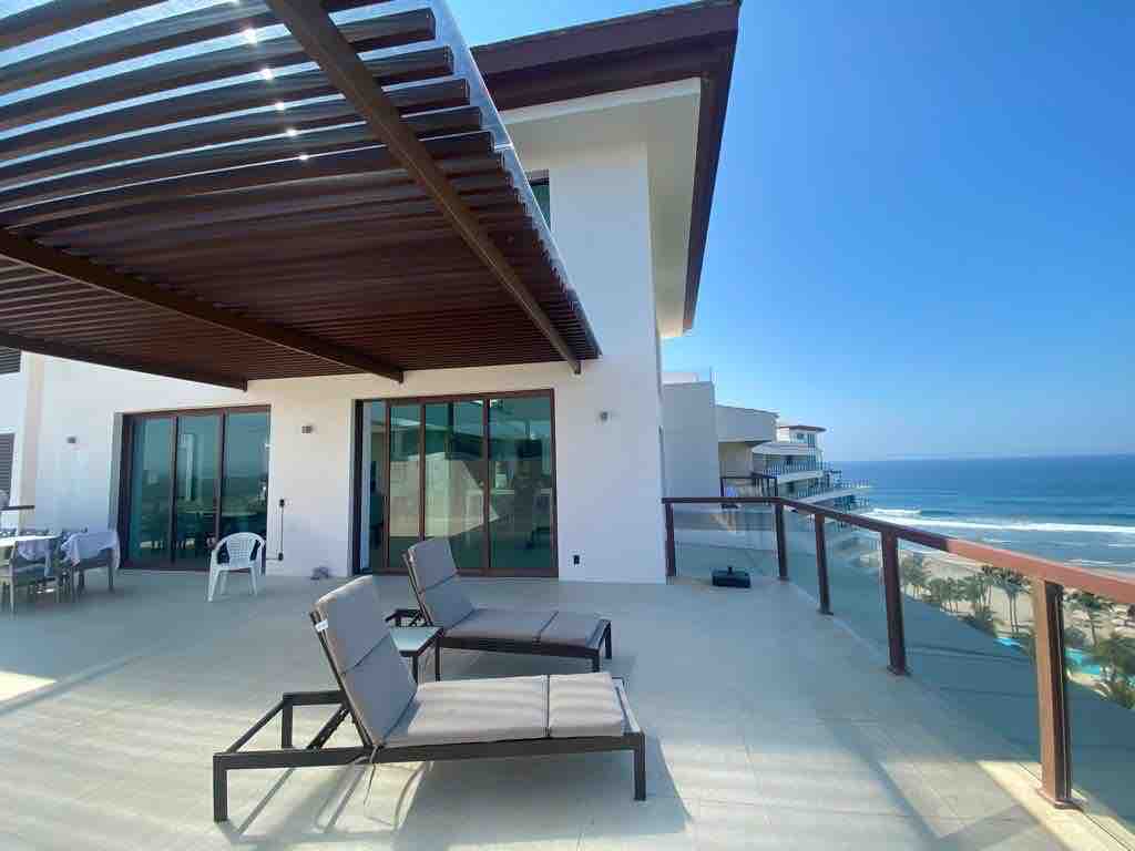 A spacious terrace features comfortable lounge chairs arranged for relaxation, offering expansive views of the ocean. Sliding glass doors provide access to the interior. Sunlight fills the area, highlighting the modern architecture and outdoor space.