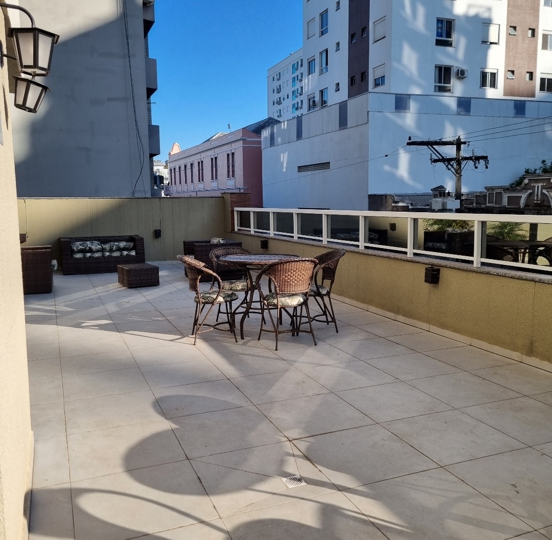 A spacious outdoor terrace is visible, featuring several wicker chairs surrounding a matching table. The floor is tiled, and large windows reflect the surrounding buildings, creating an open and inviting space for relaxation and socializing.
