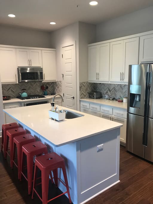 A bright white kitchen with quartz countertops and stainless appliances.