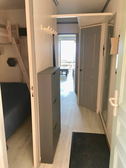 Entrée de l’appartement avec meuble à chaussures, portes-manteau, porte clés, espace de rangement des valises en hauteur. A gauche entrée sur la chambre.