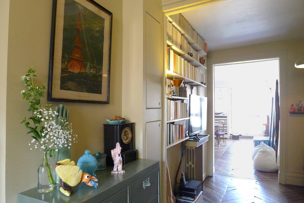 Un joli dégagement meublé habillé de livres entre la chambre, la cuisine et le salon. Dans un renfoncement à la droite de l'image se trouve le canapé convertible.