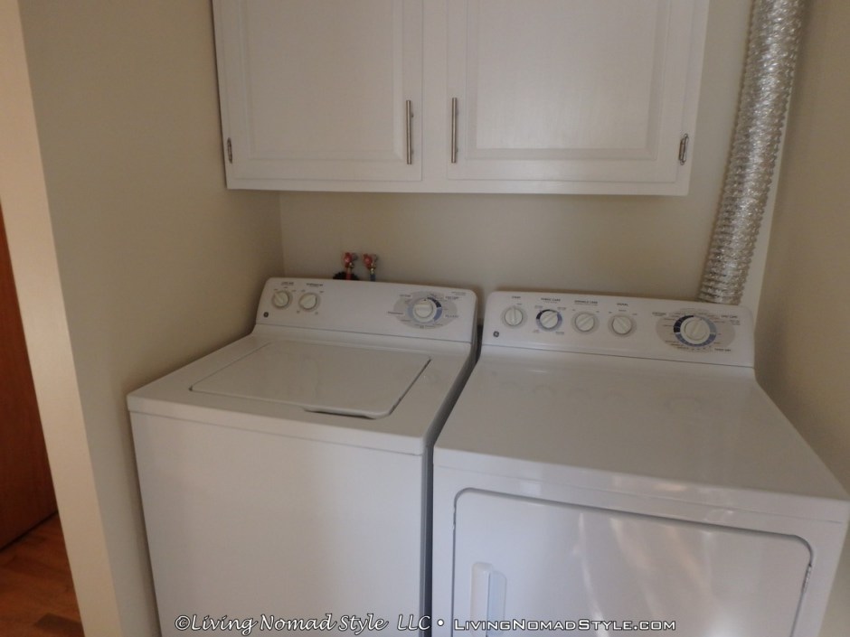 A laundry area features a stacked washer and dryer, both in white finish, positioned against a neutral wall. Above, cabinets offer additional storage, providing a functional space for laundry needs.