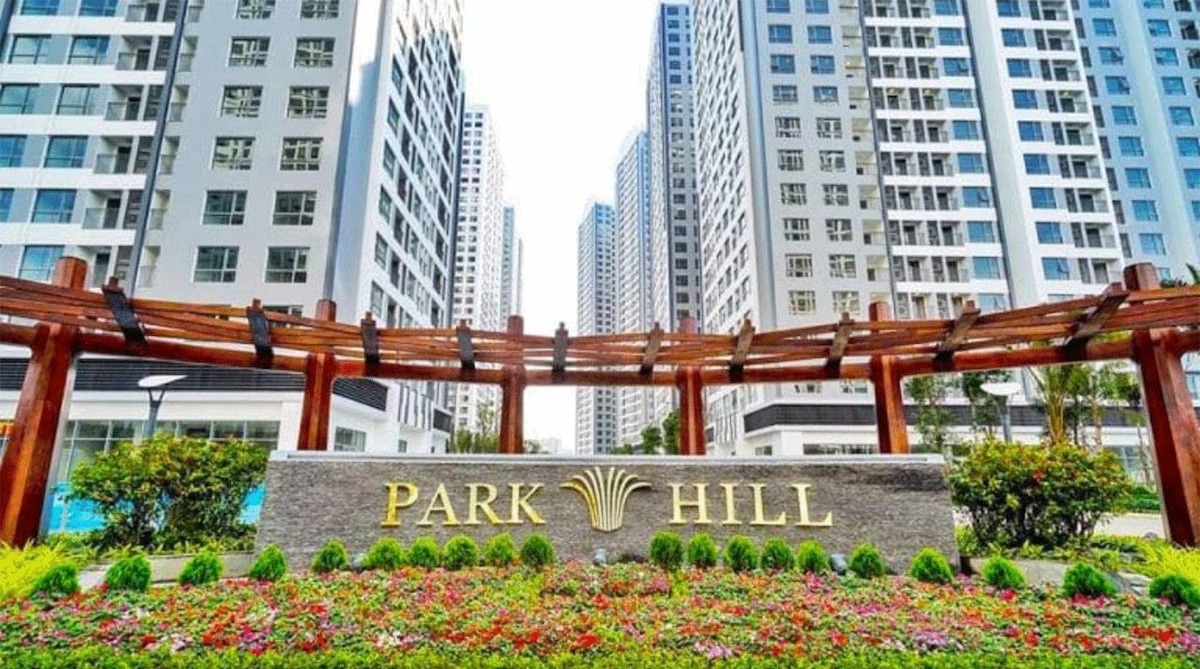 A welcoming entrance to Park Hill is highlighted, showcasing a stone sign featuring the name 'PARK HILL'. Vibrant flowers are planted in front, complemented by a wooden trellis structure above. Surrounding the entrance are modern high-rise buildings, contributing to a lively atmosphere.