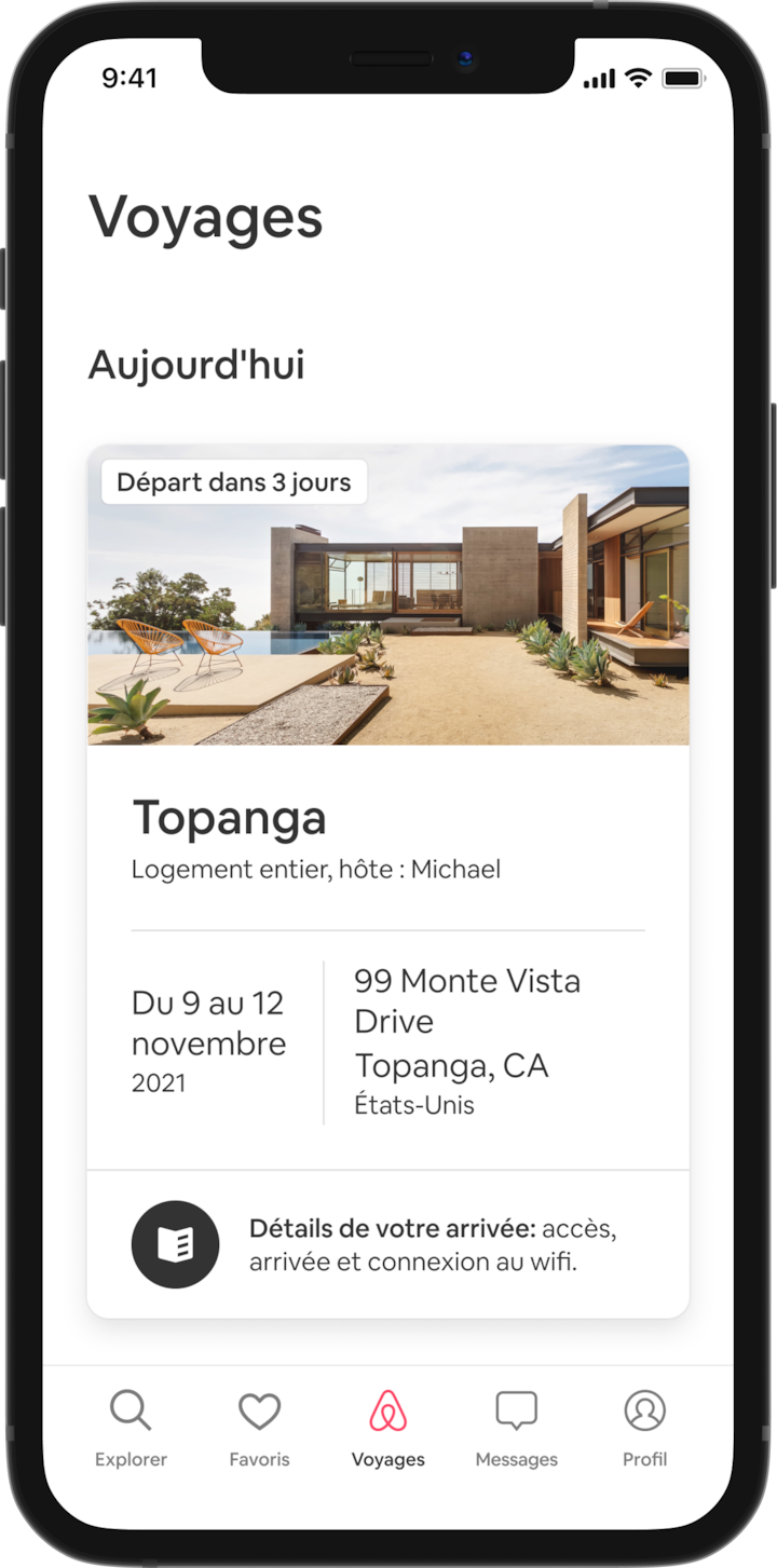 Un téléphone mobile affiche un voyage à venir dans l'onglet Voyages d'un voyageur. Sous le titre « Aujourd'hui », on peut voir l'image d'un chalet triangulaire, et en dessous, les détails de la réservation du voyageur (le nom de l'annonce, le nom de l'hôte, l'adresse et les dates du voyage). En bas de l'écran se trouve un bouton indiquant : « Informations sur l'arrivée. Indications d'accès, procédure d'entrée et connexion au wifi ».