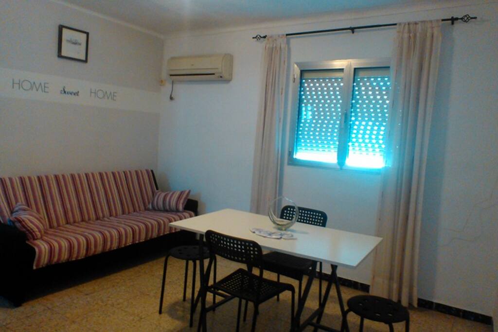 Sitting room with sofa bed, air conditioner, table and chairs.