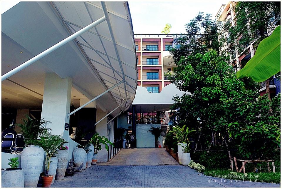 The entrance to the residence features a welcoming pathway lined with potted plants and greenery. A modern building facade showcases a blend of architectural elements, while the overhang provides shelter for guests. The surrounding area is well-maintained and invites exploration.