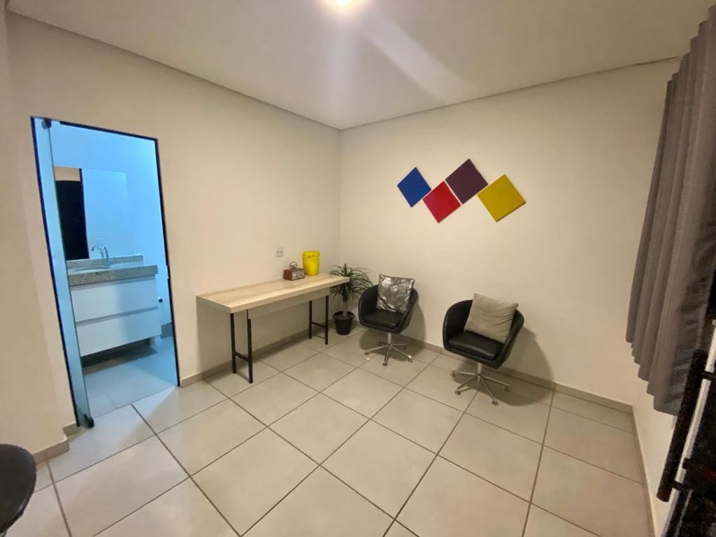 A spacious lounge area is presented with two black chairs positioned beside a minimalistic table. Colorful wall art in shades of red, yellow, and blue adds a pop of color to the neutral backdrop. Natural light filters in through a nearby window, enhancing the ambiance.