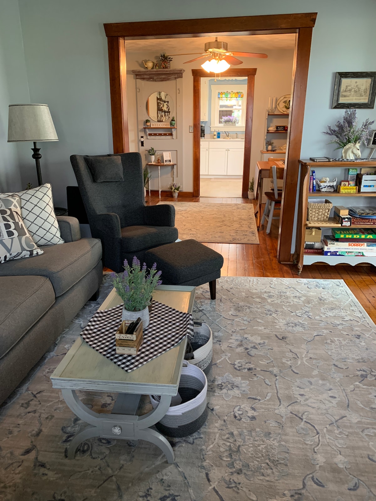 A well-appointed living area showcases a comfortable sofa and a cozy armchair. A decorative table in the center is adorned with a vase of lavender and patterned accessories. The space leads to a bright dining area, with warm wood accents enhancing the inviting atmosphere.