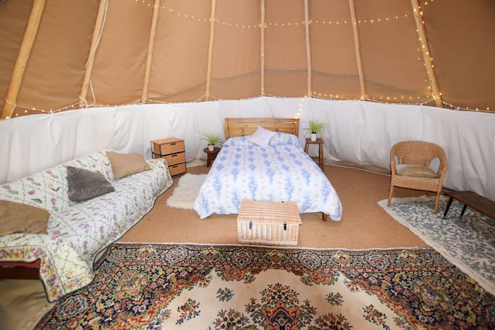Dentro del gran Tipi de 21 pies hay una cama doble, sofá, silla, cajones, cesta de picnic, riel colgante, caja fría, alfombras, ropa de cama y camas de piso adicionales si es necesario.