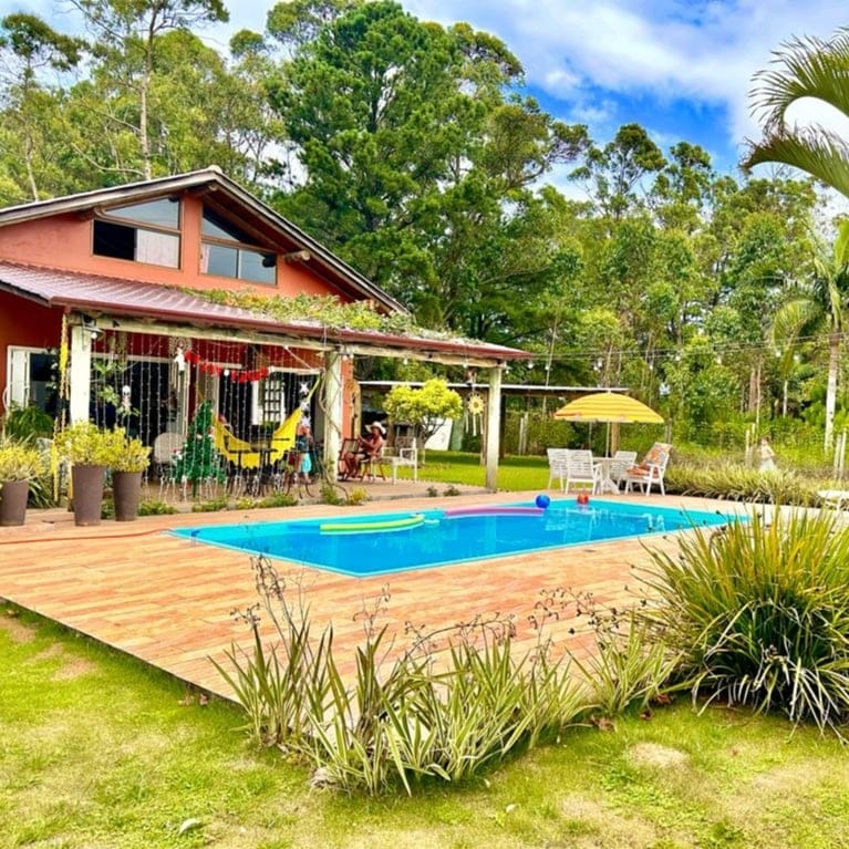A private pool area is featured in the backyard, surrounded by well-kept greenery. Lounge chairs and an umbrella provide comfortable seating options, while a spacious wooden deck allows for relaxation. The home has large windows that blend the outdoor space with the interior.