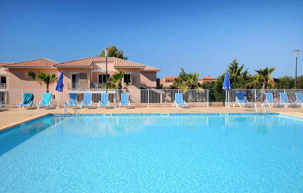 A clear blue outdoor pool is surrounded by sun loungers and umbrellas, providing a relaxing area for guests. The pool is framed by well-maintained landscaping, with charming buildings visible in the background, creating a welcoming atmosphere.