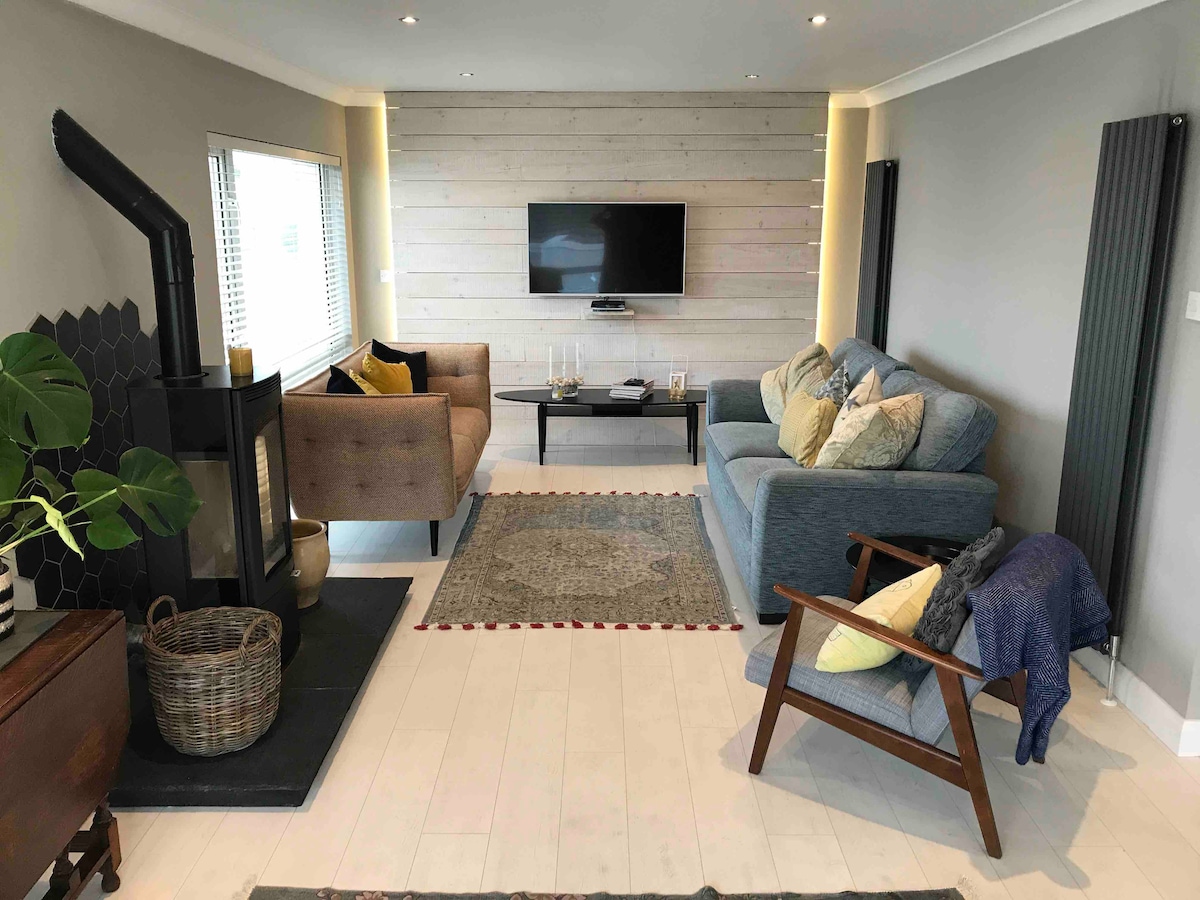 Sala de estar con estufa de leña .
Sofás cómodos , televisor inteligente grande.
Plan abierto a la cocina de diseño moderno.