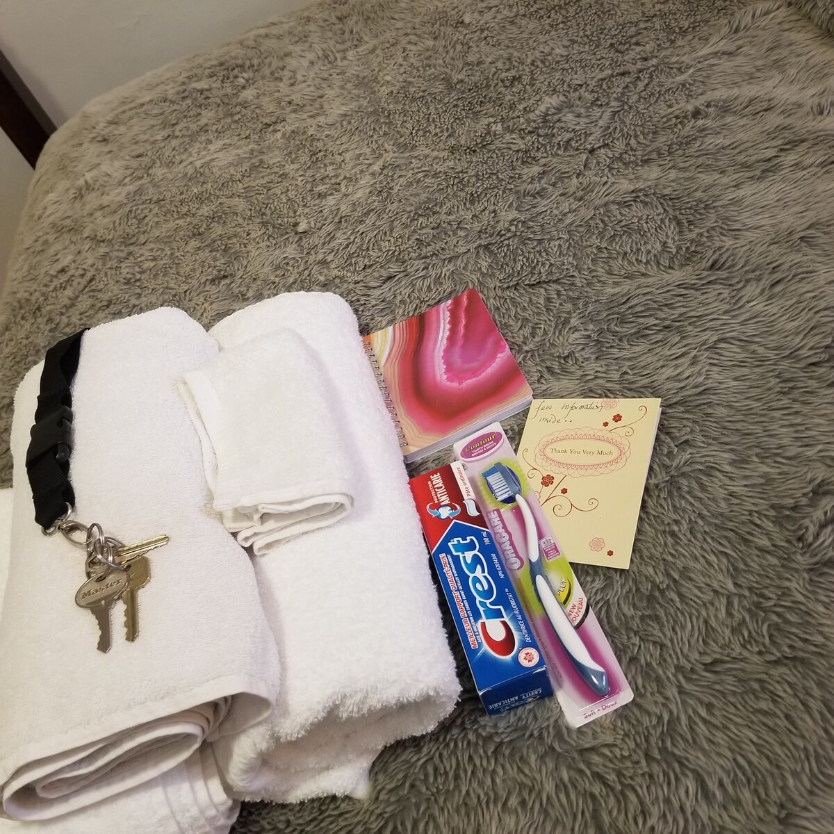 A neatly arranged collection of fresh towels sits atop a soft, textured surface. Personal care items include a toothbrush and toothpaste, along with a decorative note, creating a welcoming touch for guests.