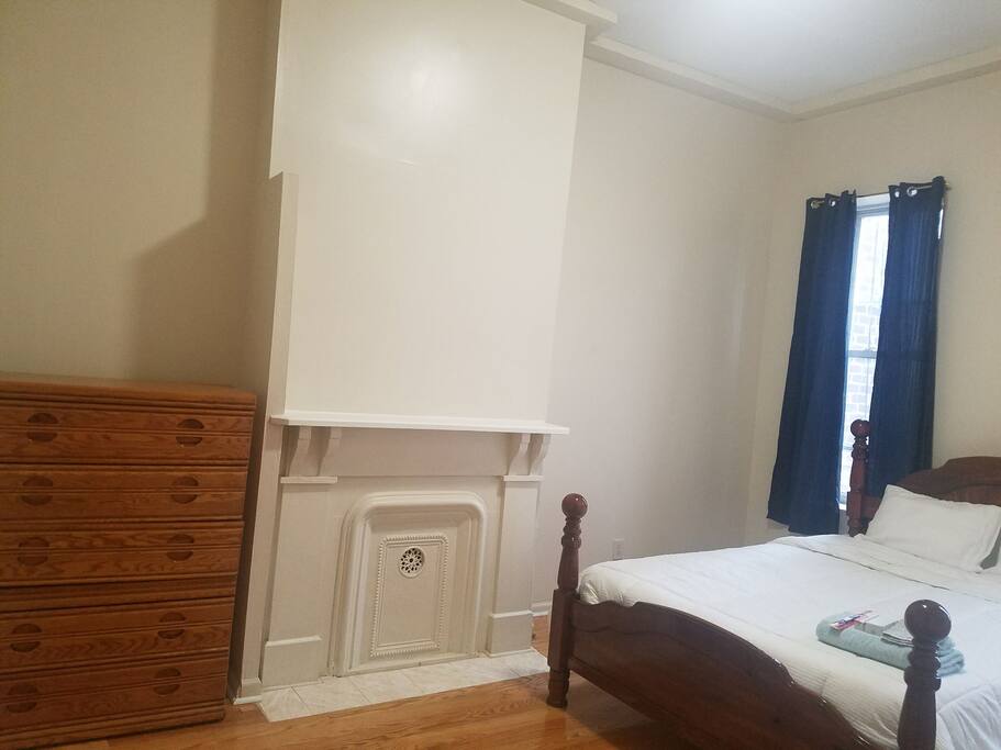 Room door view of Queen bed, 1 of 2 tall windows, beautiful mantle and 5 drawer wooden chest