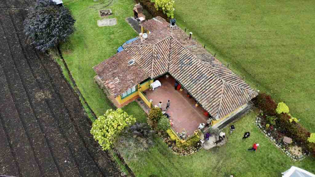 An aerial view captures the spacious finca, featuring a traditional tiled roof and open outdoor areas surrounded by greenery. Lush garden spaces and a cultivated field are visible, demonstrating the connection to nature and tranquility of the countryside.