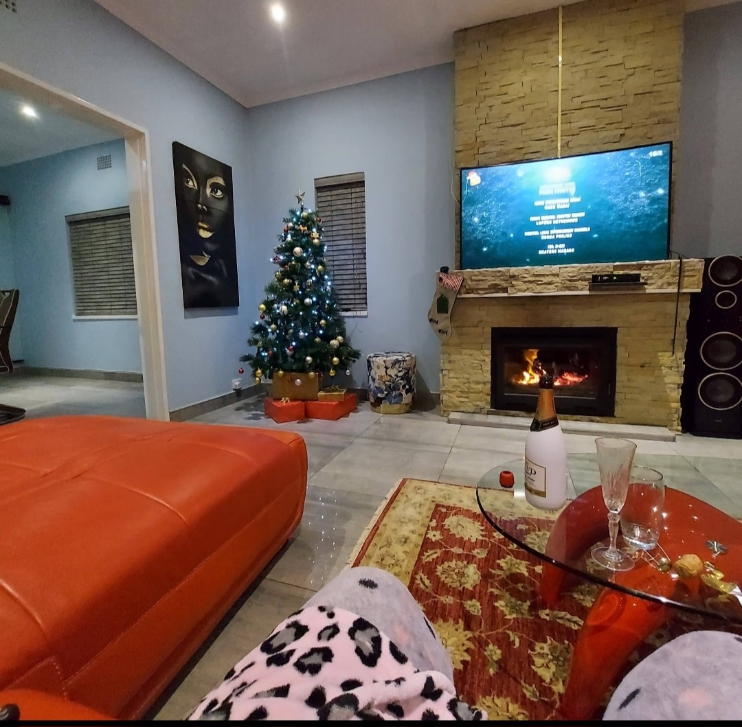 A cozy living area is presented with a vivid red sectional couch and a stylish glass coffee table. A decorated Christmas tree stands in one corner, while a modern fireplace is positioned beneath a large television screen. Ambient lighting enhances the inviting atmosphere.
