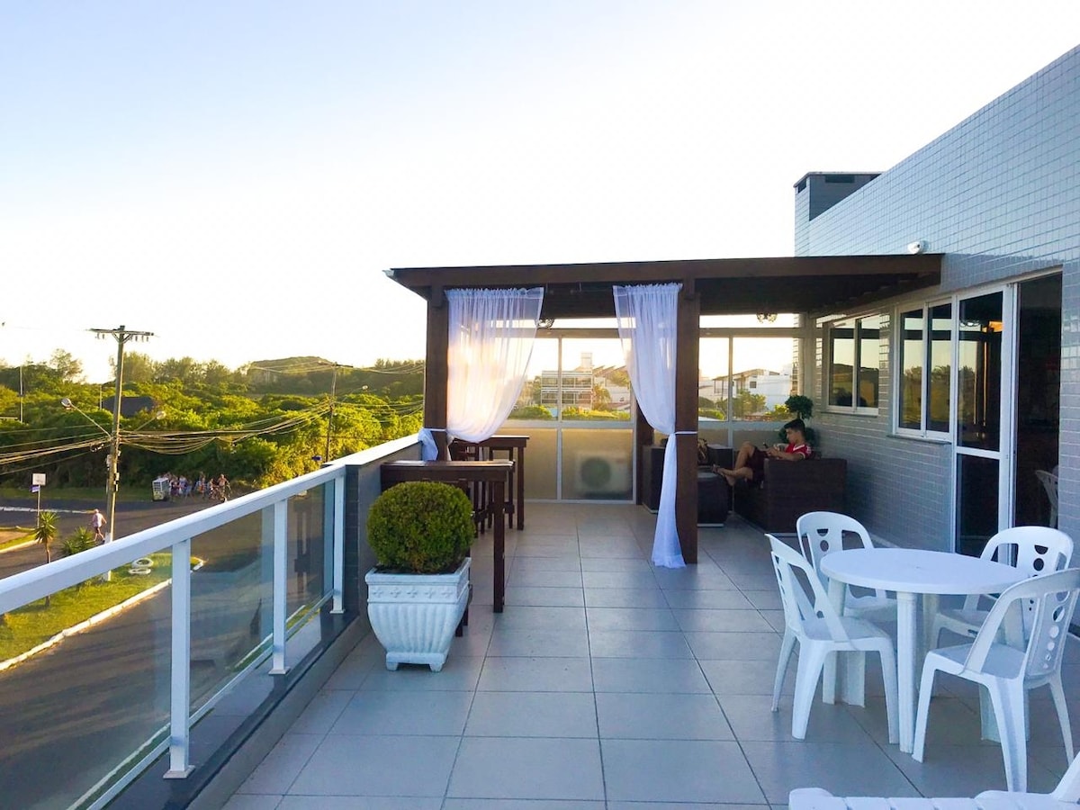 A spacious terrace is featured, offering outdoor seating arrangements with a table and chairs. Sheer curtains gently sway in the breeze, framing scenic views of the surrounding landscape. A lounge area is included, with comfortable seating, enhancing the space for relaxation.