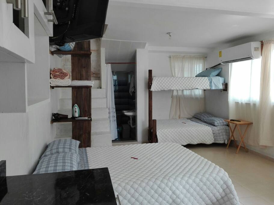 Cama matrimonial, televisor, repisas con cobijas, toallas, plancha y secadora de pelo, entrada para el baño y litera.