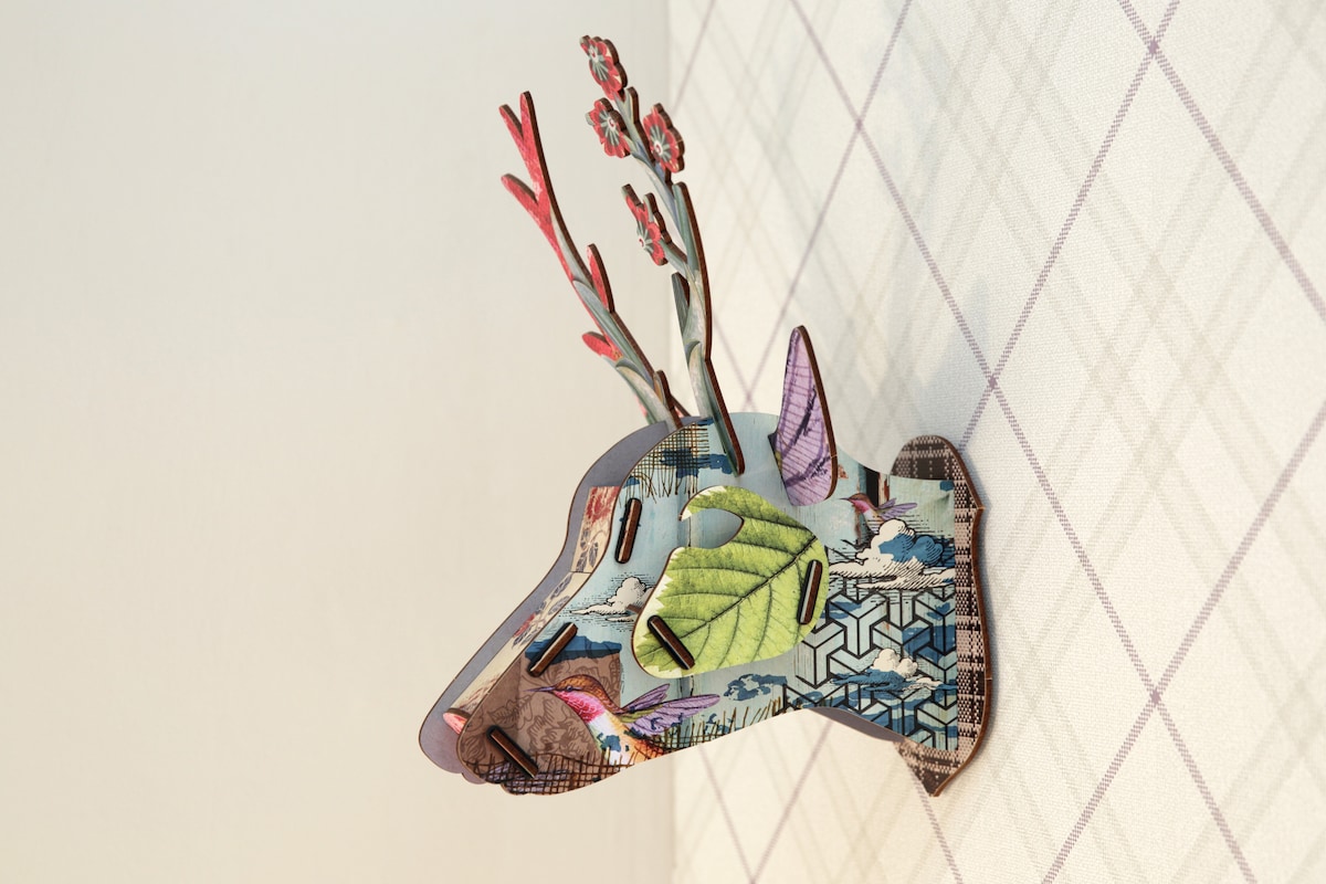 A decorative wall sculpture of a deer head is affixed to the wall, featuring intricate designs in vibrant colors. Floral elements and geometric patterns create a playful contrast against the muted background of the wall.