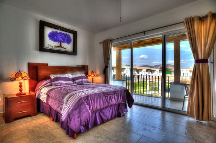 חדר שינה ראשי עם מיטת קווין סייז אחת. מרפסת המשקיפה על הבריכה, עם שולחן וכיסאות כדי ליהנות מרגע שקט.