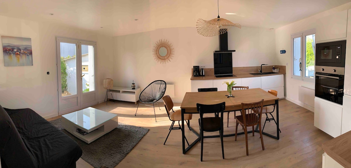 A modern open-plan living area is visible, featuring a spacious dining table surrounded by various chairs. A comfortable seating area includes a dark sofa and a glass coffee table. Large windows allow natural light to fill the space, enhancing the neutral color palette.