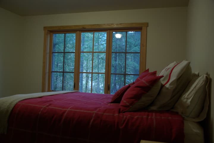 Главна спална соба на долниот кат со брачен кревет и шумски поглед.  
