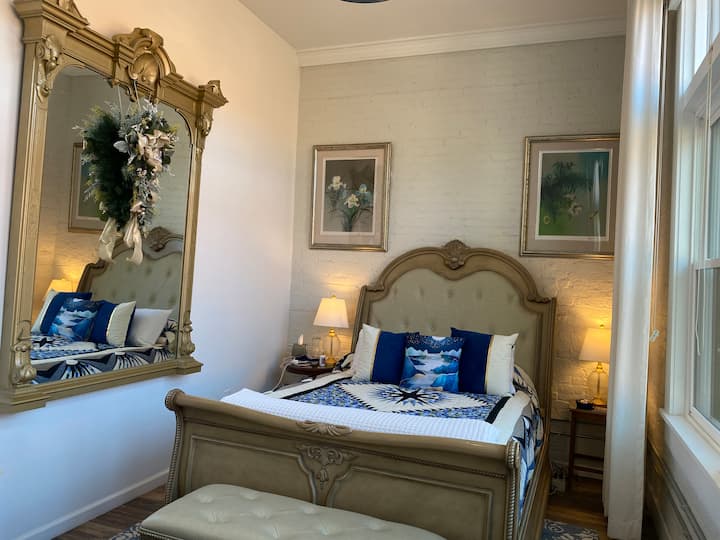 غرفة نوم تضم سرير كوين مع مرتبة لضبط الرأس والقدم، ومرآة رصيف عتيقة أصلية للمبنى منذ أكثر من 100 عام، وستائر وستائر كاملة الطول، وتلفزيون ذكي، وخزانة ملابس، وخزانة ملابس، ومكتب، وفن أصلي.