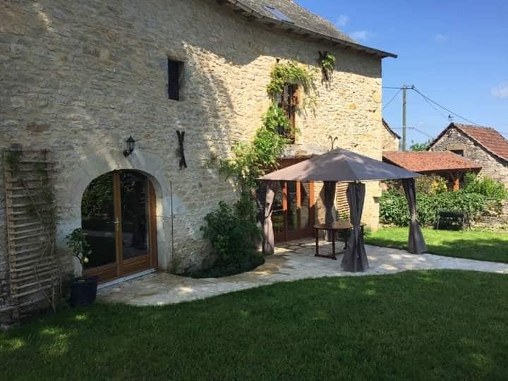 A charming stone barn features a spacious outdoor area with a gazebo and table. Green vines adorn the building's exterior, and a well-maintained lawn surrounds the setting. Large glass doors lead into the interior, offering a seamless connection with the outdoor space.