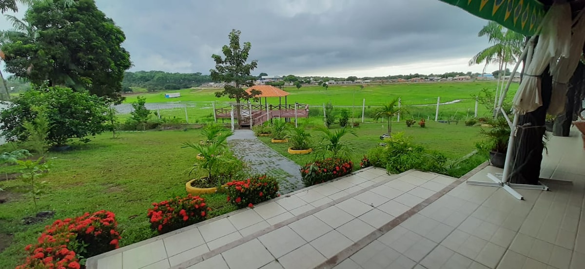 A well-maintained outdoor area showcases lush green grass and vibrant flower beds, bordered by a pathway leading to a gazebo overlooking the lake. The scene is set beneath an overcast sky, enhancing the tranquil atmosphere of the surrounding landscape.