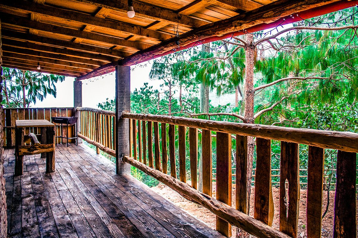 A wooden deck is surrounded by pine trees, providing a serene outdoor space. A simple table and two chairs are positioned on the deck, allowing for peaceful relaxation. The wooden railing offers a rustic touch, enhancing the natural surroundings.