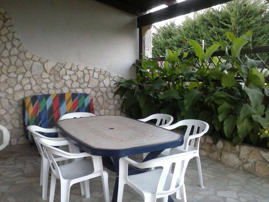 Spazio Esterno Coperto da Veranda in Legno , dove si trova Tavolo con Sedie , Divano , Lavatrice e TV.