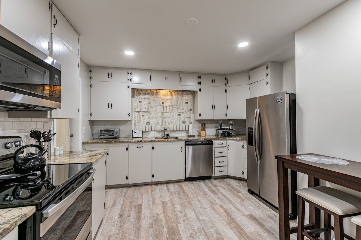 A modern farmhouse style kitchen is presented, featuring granite countertops and stainless steel appliances, including a refrigerator, stove/oven, dishwasher, and microwave. Ample storage cabinets and a stylish backsplash enhance the space. A small wooden table with seating is also visible.