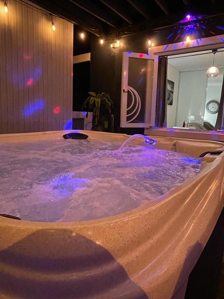 An inviting jacuzzi is illuminated by colorful lights, creating a relaxing atmosphere. The bubbles rise gently in the water, while the surrounding space features modern decor and large windows that provide a view of the room beyond.
