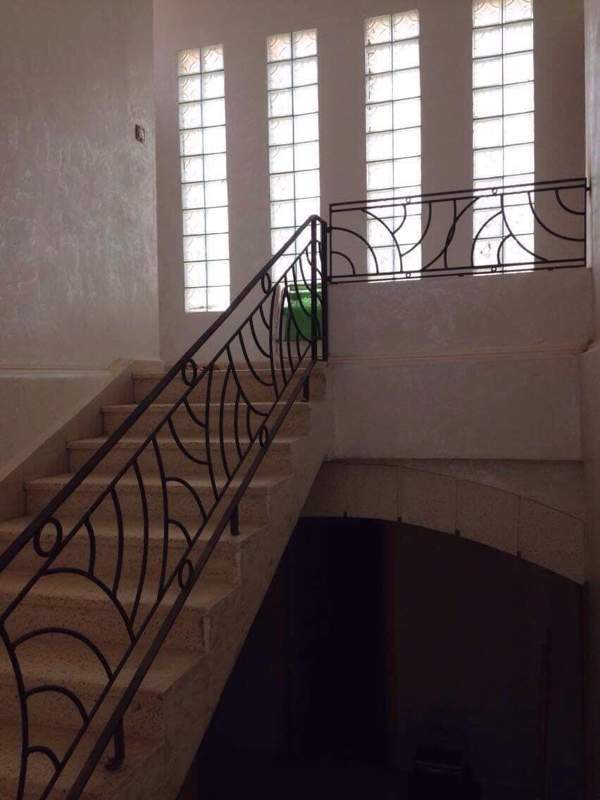 Stairs with a decorative metal railing lead to an upper level, illuminated by natural light filtering through large glass block windows. The walls are finished in a light color, contributing to a bright and open atmosphere.
