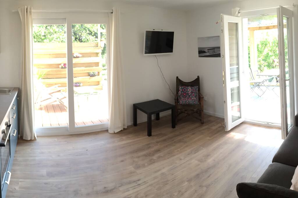 Joli salon-cuisine avec ses deux petites baies vitrée donnant sur une terrasse bois et une petite terrasse en pierre couverte.