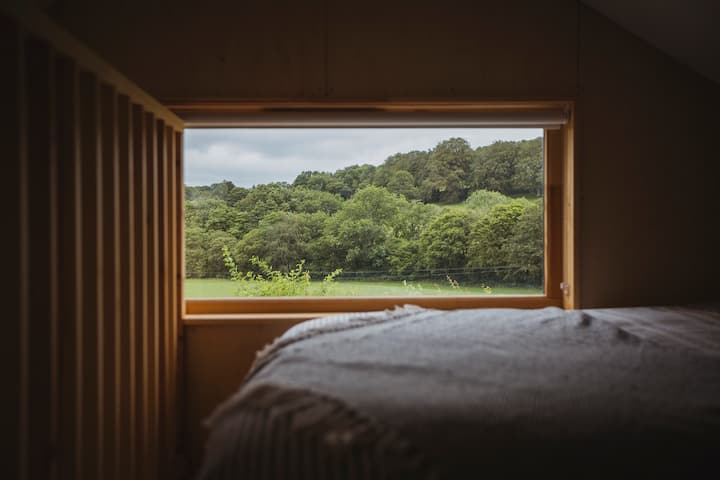 לופט השינה בקרוגלופט כולל מיטה זוגית וחלון תמונות המשקיף על שדות אורגניים.