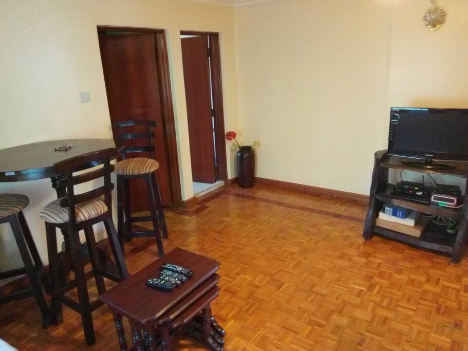 View from the couch with TV and Zuku/DSTV decorders. Doors to the bedroom and kitchenette from left to right respectively.
