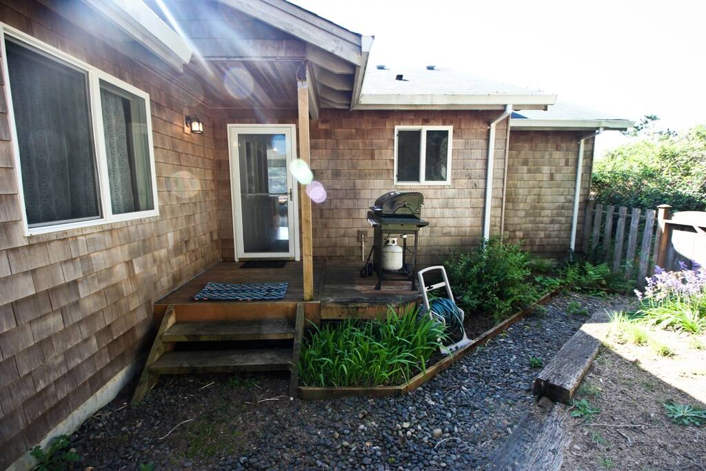 Fenced backyard with deck, gas BBQ and gravel pathway around the house