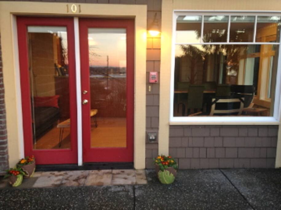 The Studio's main entrance, with sunset reflected in the glass. Summertime brings outdoor furniture for seating with a bay view.