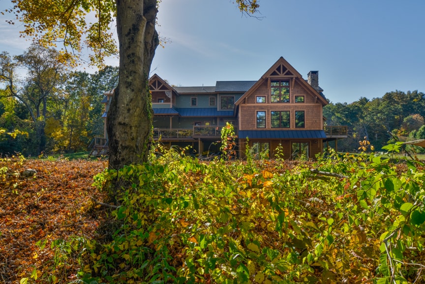 The exterior of the lodge is set against a backdrop of vibrant autumn foliage. The structure features multiple levels with large windows that enhance the natural light. A spacious deck extends from the building, inviting outdoor relaxation in a serene, wooded setting.