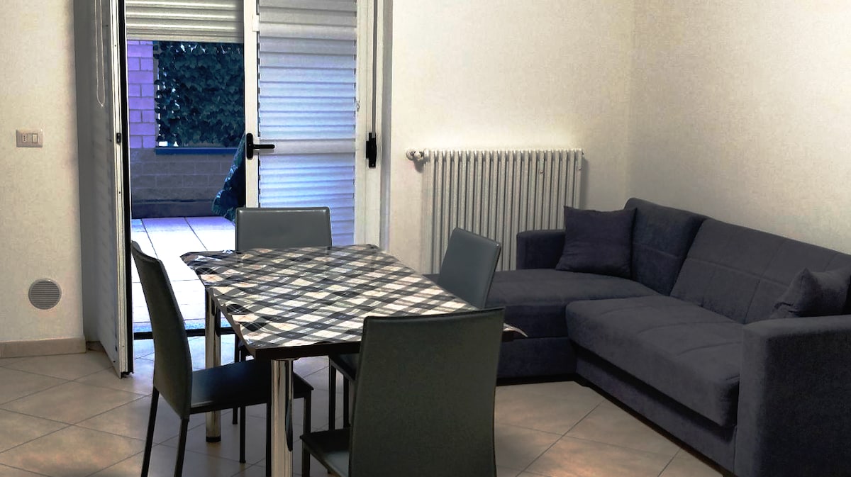 A spacious living area features a dark gray sectional sofa and a dining table set for six, adorned with a checkered tablecloth. A sliding glass door provides access to an outdoor patio, letting in natural light and offering views of a private courtyard.