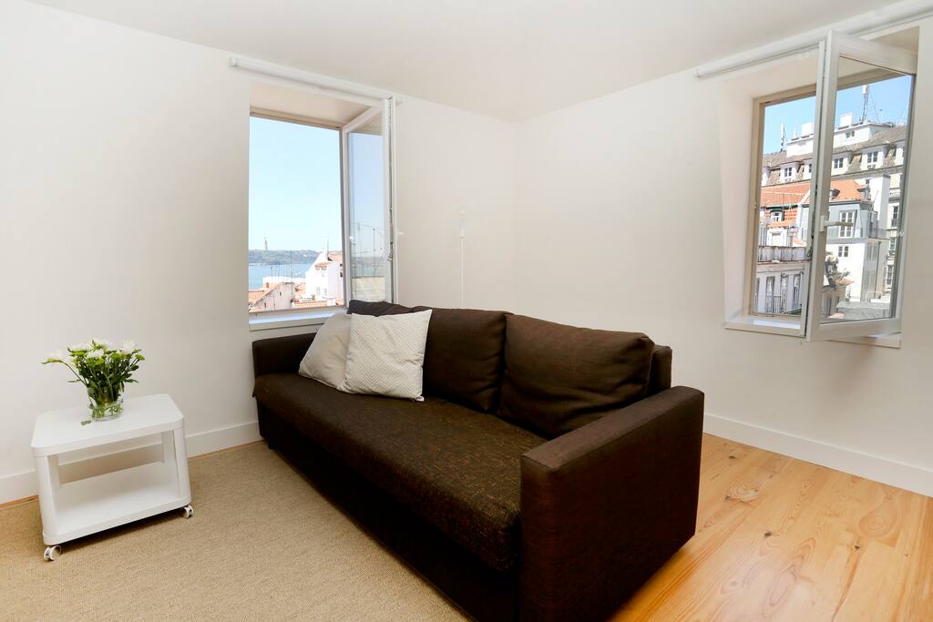 a sofa-bed in the living room; Windows with view to the historic center roofs and the Tagus River, plenty of natural light