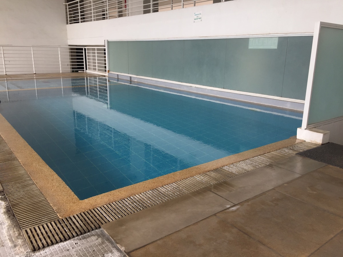 An indoor swimming pool is visible, featuring clear blue water reflecting natural light. The pool area is surrounded by smooth tiles and has a minimalist design, with frosted glass panels providing an element of privacy and safety.