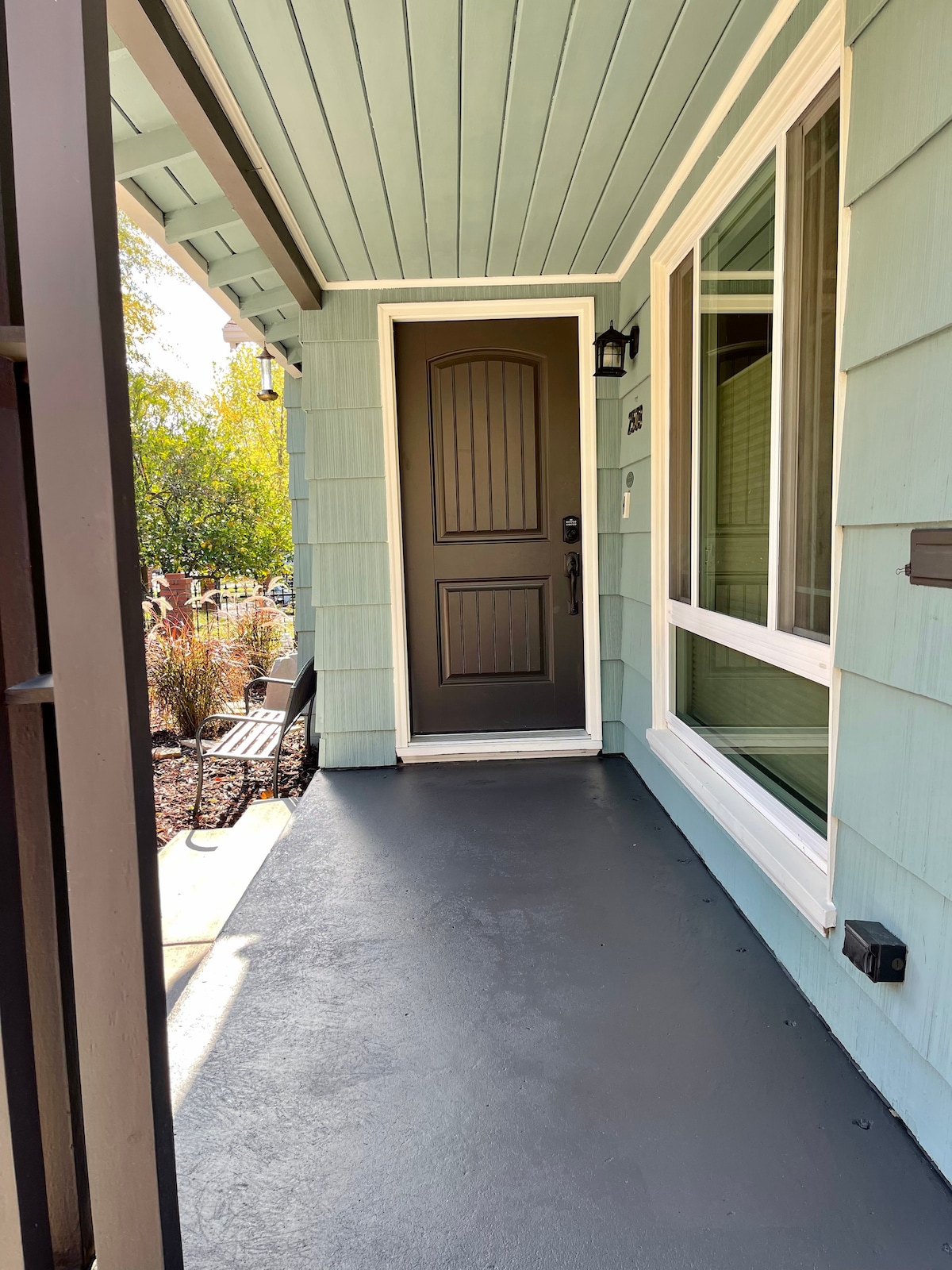 The entryway features light teal siding and a dark front door with a decorative panel. A porch with smooth flooring is visible, along with a window beside the door, allowing natural light to illuminate the space.