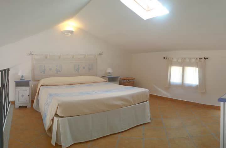 Loft with comfortable double bed. Bedside lamps, headboard, and bedspread are pieces of Sardinian craftsmanship. 