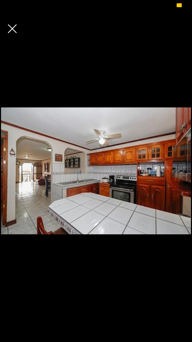 A spacious kitchen features wooden cabinetry and a tiled island with seating. Stainless steel appliances are neatly arranged, while natural light enters through the window. An archway leads to the adjoining living area, enhancing the open layout.