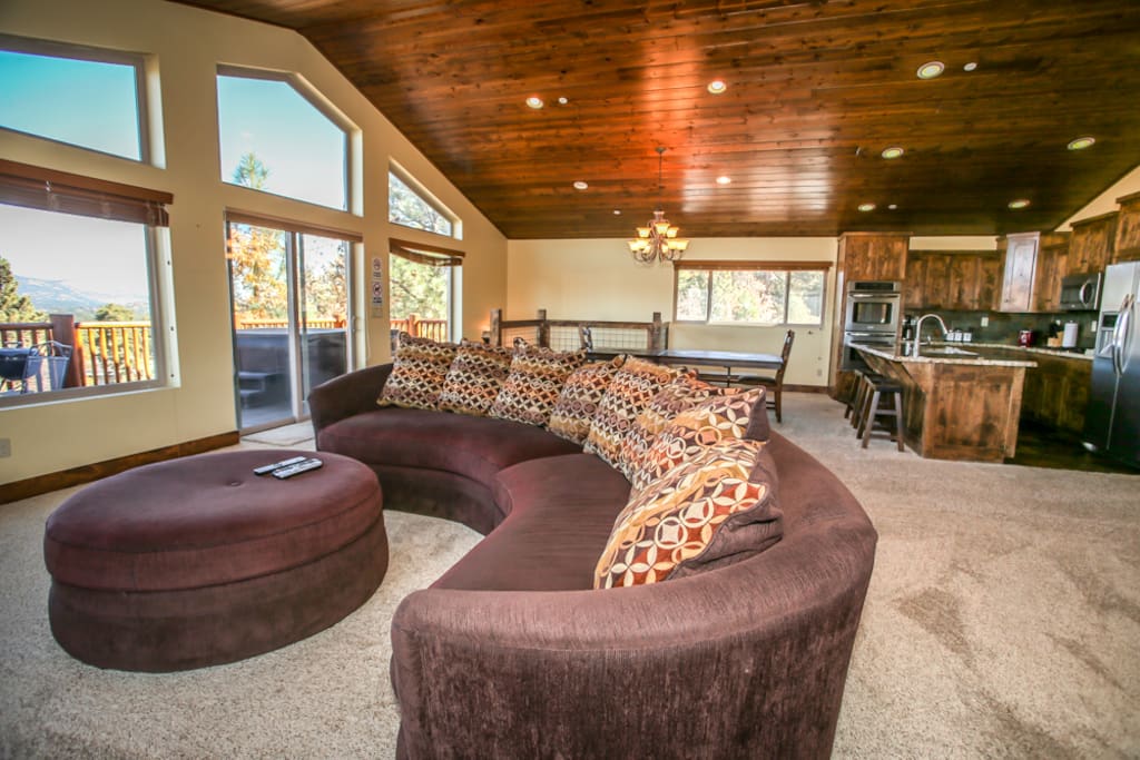This room features gorgeous views of all of Big Bear! You can see the alpine slide, Big Bear Blvd, the lake, and the mountains! This room is also great for large groups. A beautiful, modern kitchen and bar can been seen in the background.