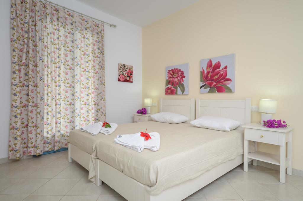A serene guest room is presented with two beds, each adorned with soft linens. Floral artwork hangs on the light-colored walls, while bright curtains frame a window. Nightstands with lamps add a functional touch to the inviting space.
