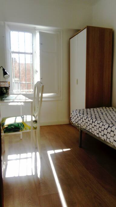 Habitación individual con escritorio, ropero, silla y lámparas.